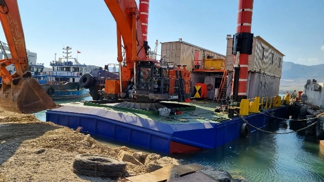 Excavator on a blue dredging pontoon at a harbour